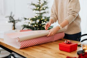 Person wrapping gifts near a Christmas tree, representing holiday joy.